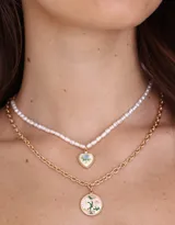 Collar corto doble de metal dorado, con una cadena de perlas y dije de corazón con flores esmaltadas, y otra cadena con dije redondo con flores esmaltadas.