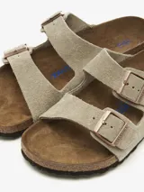 Sandalias Birkenstock Arizona de cuero gamuzado color topo, con dos correas ajustables con hebillas metálicas color cobre y plantilla anatómica de corcho y látex.