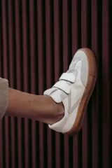 Zapatillas urbanas blancas con detalles en gris y suela color caramelo. Presentan cierre con tiras de velcro.