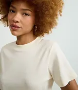 Blusa básica de manga corta y cuello redondo, color blanco hueso, confeccionada en algodón sostenible.