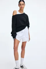 Buzo negro con escote off-the-shoulder, hombros caídos, corte holgado y mangas largas con puños acanalados.