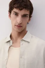 Camisa de lino color crema, de corte recto, con cuello inglés, tapeta clásica, mangas largas con puños abotonados y bajo redondeado.