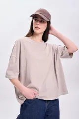 Remera beige de corte holgado con cuello redondo y mangas cortas. Presenta pequeños apliques brillantes dispersos en el frente.