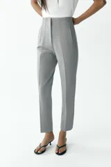 Pantalón gris de tiro alto con costuras marcadas en delantero y espalda, bolsillos delanteros de vivo y cierre frontal con cremallera, botón interior y gancho metálico.