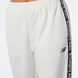 Pantalón deportivo New Balance Performance Fleece para mujer, color blanco, con cintura elástica, corte holgado y logo de la marca en la pierna izquierda. Presenta una banda lateral con la inscripción "New Balance" repetida en negro.
