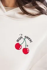 Canguro de felpa color crema, de corte oversize, con capucha y bolsillo tipo canguro. Tiene un pequeño bordado de cerezas en el pecho.