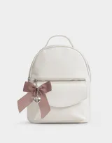 Mochila pequeña de cuero sintético color blanco con bolsillo frontal con solapa y cierre superior. Incluye un charm colgante de moño a rayas rojas y blancas con dije de corazón plateado.