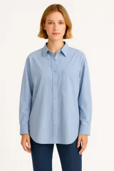 Camisa celeste de algodón, de corte holgado, con cuello clásico, cierre frontal con botones, bolsillo de parche en el pecho y mangas largas con puños abotonados.