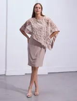 Vestido de fiesta color beige, de corte recto y largo a la rodilla, confeccionado en seda fría. Presenta una sobrecapa de microtul bordado con motivos florales.