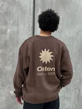 Buzo marrón con logo "Osten" y diseño gráfico de sol en color beige. Corte oversize, cuello redondo y mangas largas.
