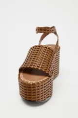 Sandalias con plataforma tipo cuña color marrón, con cuerpo trenzado, tira delantera y cierre mediante tira con hebilla a la pulsera del tobillo.