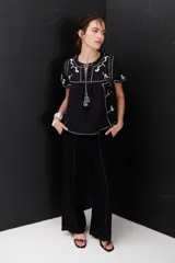 Blusa negra con bordados blancos de animales y motivos geométricos. Tiene cuello redondo con lazo y mangas cortas.