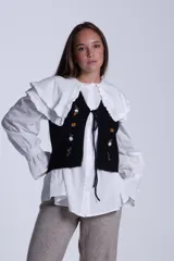 Chaleco tejido color crema con escote en V y cierre frontal con lazos. Presenta bordados de flores en tonos naranja, verde y blanco.