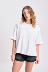 Remera blanca de corte holgado con cuello redondo y mangas cortas, terminaciones con pespunte rojo.