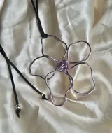 Collar con dije de flor hecho con alambre color lila y cordón negro.