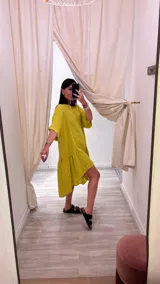 Vestido corto color fucsia, de lino, con cuello redondo y mangas cortas. Es más corto adelante que atrás, con corte transversal en la falda.