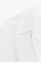 Camisa blanca de cuello solapa y manga larga con puños. Tiene un nudo en la parte delantera y cierre frontal con botones.