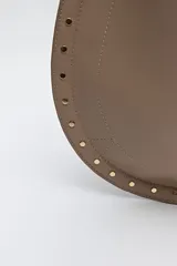 Bolso hobo color beige de símil cuero con textura suave y tachas metálicas en los bordes. Tiene correa al hombro y logo metálico en el frente.