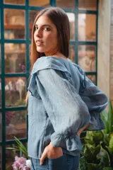 Blusa celeste de algodón con mangas largas abullonadas y puños elastizados con volados. Presenta volados en los hombros y escote redondo.