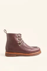 Bota de cuero vacuno color bordó con acabado brillante, diseño tipo botineta con cordones y ganchos metálicos. Presenta suela de goma tipo crepe con plataforma y costuras visibles en la puntera.