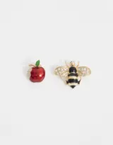 Set de dos prendedores: uno con forma de manzana roja mordida con hoja verde y detalles de strass, y otro con forma de abeja con cuerpo a rayas negras y doradas y alas con strass.