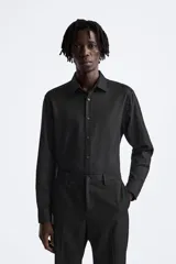 Camisa blanca de corte regular, cuello italiano, manga larga con puños abotonados y cierre frontal con botones.
