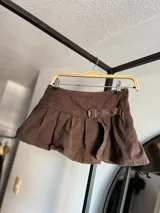 Minifalda negra de jean con tablas, abertura lateral y cinturón con hebilla metálica.