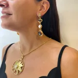 Collar con cadena dorada y dije colgante de sol con textura rugosa y una perla redonda engarzada en el centro.