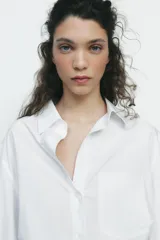 Camisa negra de cuello solapa y manga larga amplia. Tiene un bolsillo de parche en el delantero, detalle de pliegues y cierre frontal con botones.