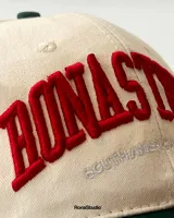 Gorra de béisbol de dos tonos, con visera curva y copa estructurada. Tiene bordado frontal en alto relieve con el texto "RONASTUDIO SOUTHAMERICAN LEAGUE".