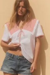 Camiseta blanca de cuello bobo con terminaciones bordadas y detalle de lazo en el delantero. El cuello y las mangas cortas son de tela a cuadros vichy color salmón.