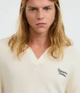 Camisa polo de hombre confeccionada en tejido de punto de algodón, color crema, con cuello en V y manga corta. Presenta un corte oversized y un pequeño bordado de lettering en el pecho.