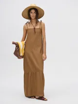 Vestido midi de denim algodón color marrón, con escote recto y tirantes finos ajustables con lazos. El corte es suelto y termina con un ruedo con semi-volado.