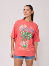 Remera color crudo de corte oversized con estampado de palmeras, flores y texto 'California' y 'Rusty Tribe'.