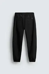 Pantalón jogger negro de corte slim fit, confeccionado en tejido de algodón con cintura elástica ajustable con cordón, bolsillos frontales y traseros de vivo, y bajo con puño elástico.