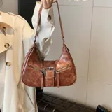Cartera marrón de eco cuero con correa de hombro ajustable y cierre con hebilla metálica.