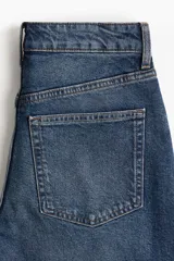 Pantalón jean azul de denim de algodón levemente elástico, corte ancho, tiro alto, largo tobillero y cinco bolsillos.