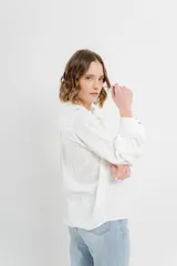 Camisa blanca de voile con bordados calados en el frente, cuello camisero, mangas largas con puños abotonados y cierre frontal con botones. 