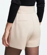 Bermuda blanca de poliéster con cintura elástica, cierre con cremallera y botones, y bolsillos laterales.