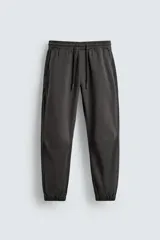 Pantalón jogger negro de corte slim fit, confeccionado en tejido de algodón con cintura elástica ajustable con cordón, bolsillos frontales y traseros de vivo, y puños elásticos en el bajo.