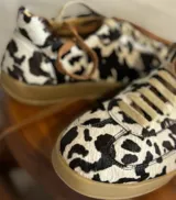 Zapatillas bajas con estampado animal print de vaca en blanco y negro, con cordones marrones y suela color caramelo.
