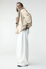 Cazadora color crudo con cuello solapa y cuello de pelo sintético desmontable, manga larga con trabillas y botones, bajo con elásticos y cierre cruzado con botones.