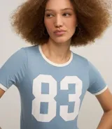 Remera baby look celeste con cuello y mangas con ribete blanco, y estampa frontal con el número 83 en blanco.