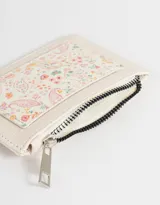 Tarjetero de cuerina con estampado floral multicolor, cierre superior con cremallera y bolsillo frontal abierto.
