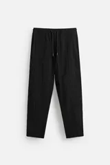 Pantalón negro de corte amplio, con textura acanalada, cintura elástica ajustable con cordón, bolsillos laterales y traseros de vivo.
