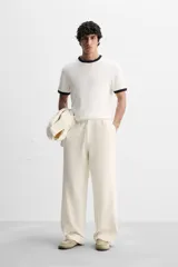 Pantalón color crema de corte amplio, con cintura elástica ajustable con cordón, bolsillos laterales y trasero, cierre frontal con cremallera y botón.