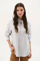 Camisa beige de corte recto, con cuello clásico, cierre frontal con botones, bolsillo en el pecho y mangas largas con puños abotonados.
