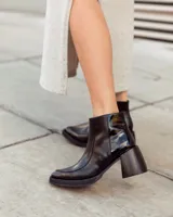 Botín corto de cuero negro, estilo cowboy moderno, con textura de cocodrilo en la caña y puntera cuadrada. Posee un tacón ancho y geométrico, y cierre lateral.