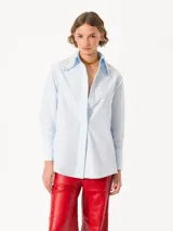 Camisa celeste de poplin, corte clásico, largo a la cadera y mangas largas. Cuello con detalle de piedras engarzadas. Cierre frontal con botones de pasta al tono.