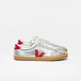 Zapatillas Veja modelo Volley, color plateado con logo lateral en rojo y contrafuerte rojo. Suela de goma color caramelo y cordones blancos.